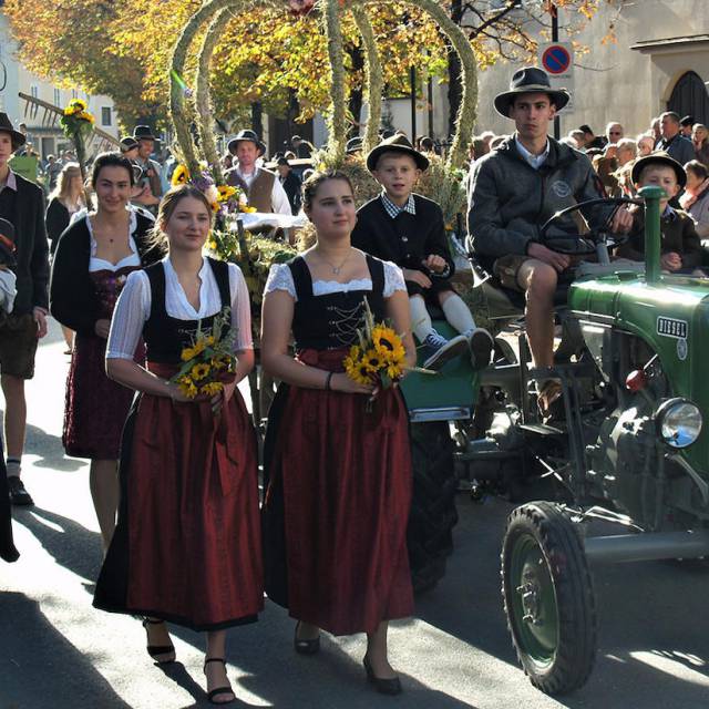 Festzug mit Dirndl, Tracht und geschmücktem Traktor bei Sonnenschein